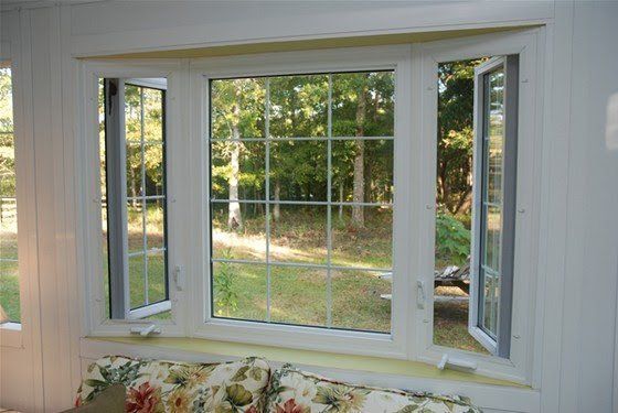 White bay window with open side windows and a floral cushion below, overlooking a leafy yard