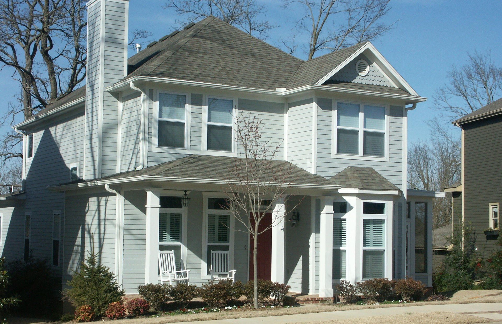 Two-story light gray house with white trim, front porch, and bare trees in the yard