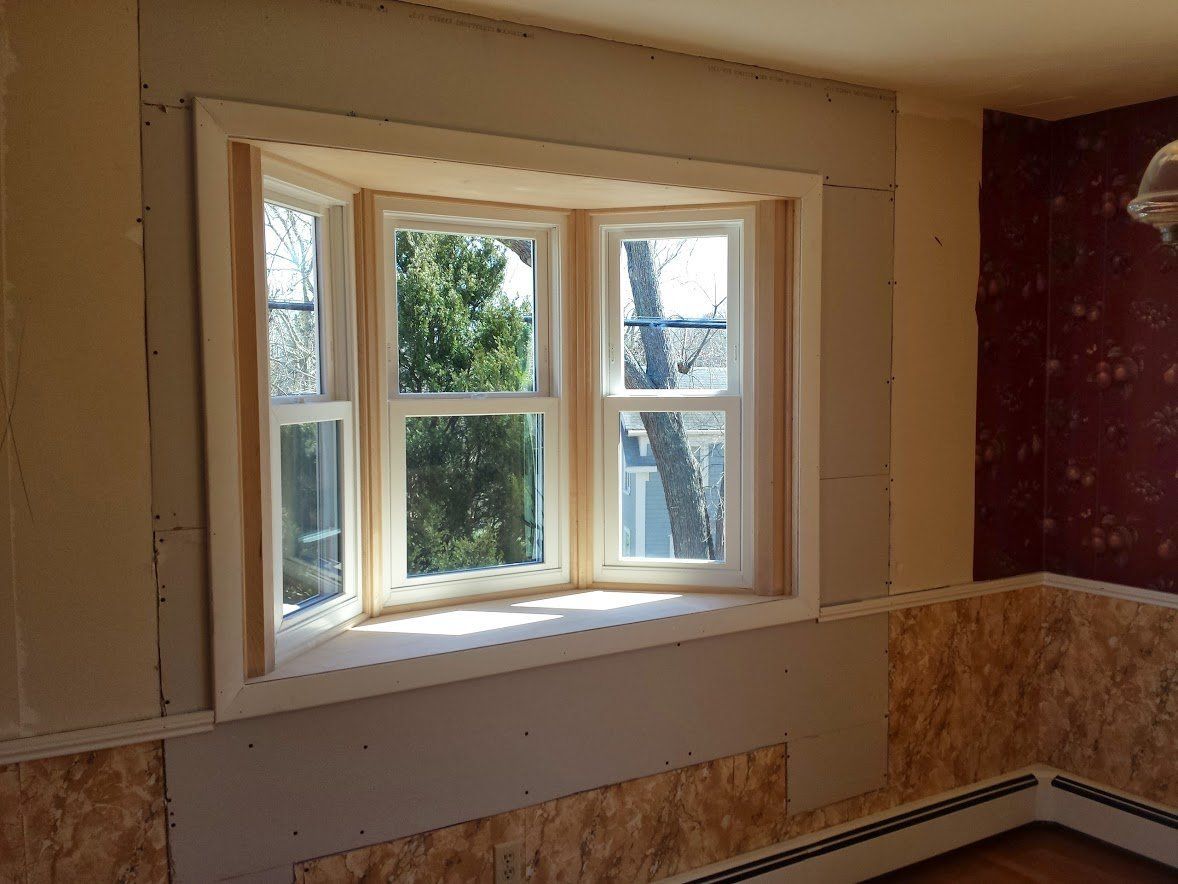 Empty room with a bay window, unfinished walls, and tiled wainscoting under renovation