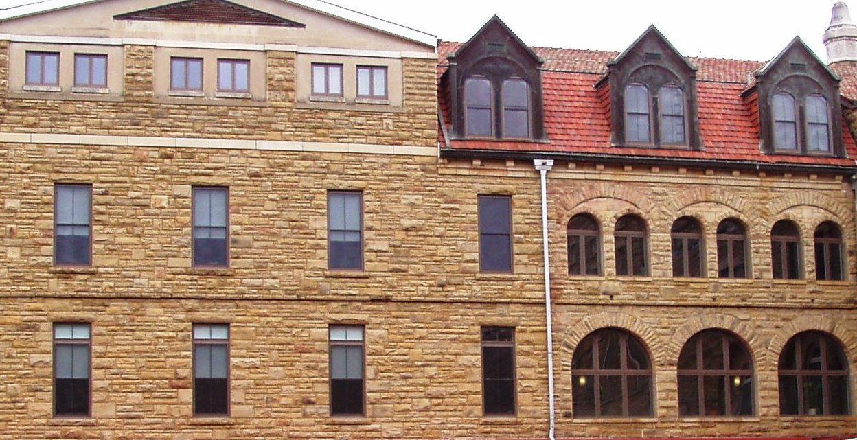 Row of brick and stone buildings with many windows and red-roofed dormers