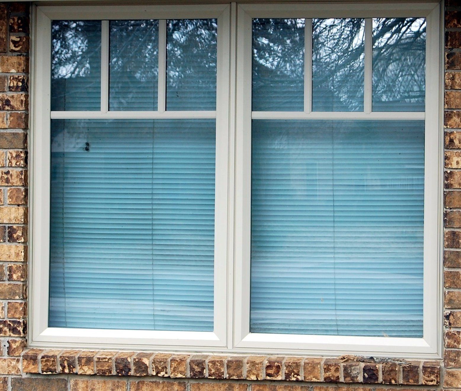 Two white-framed windows with blue blinds and a brick exterior wall around them