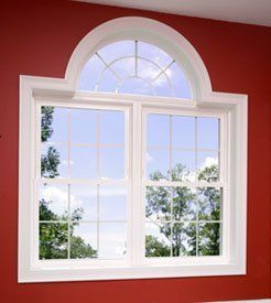 White-framed arched window with divided panes set in a red wall, showing trees and sky outside
