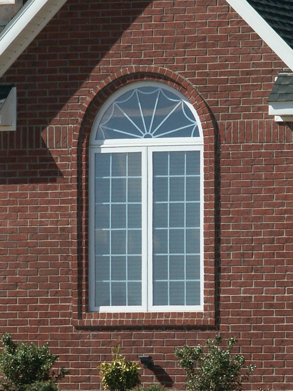 Brick house window with white trim and arched transom above it