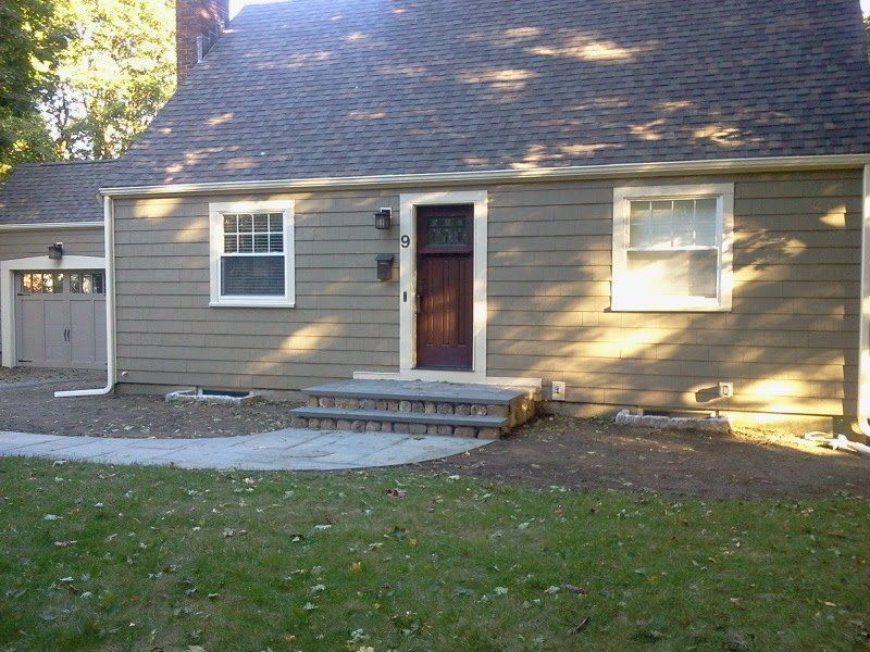 Small beige house with gray roof, front steps, and a garage at left, seen from the yard.