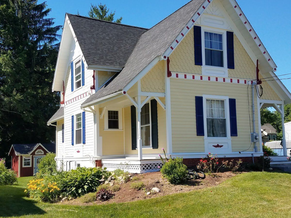 White two-story house with blue shutters and a yellow porch on a sunny lawn