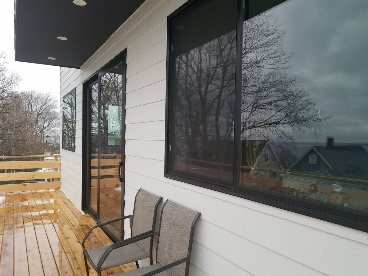 Modern porch with white siding, black-framed windows, wooden deck, and outdoor chair under an overhang