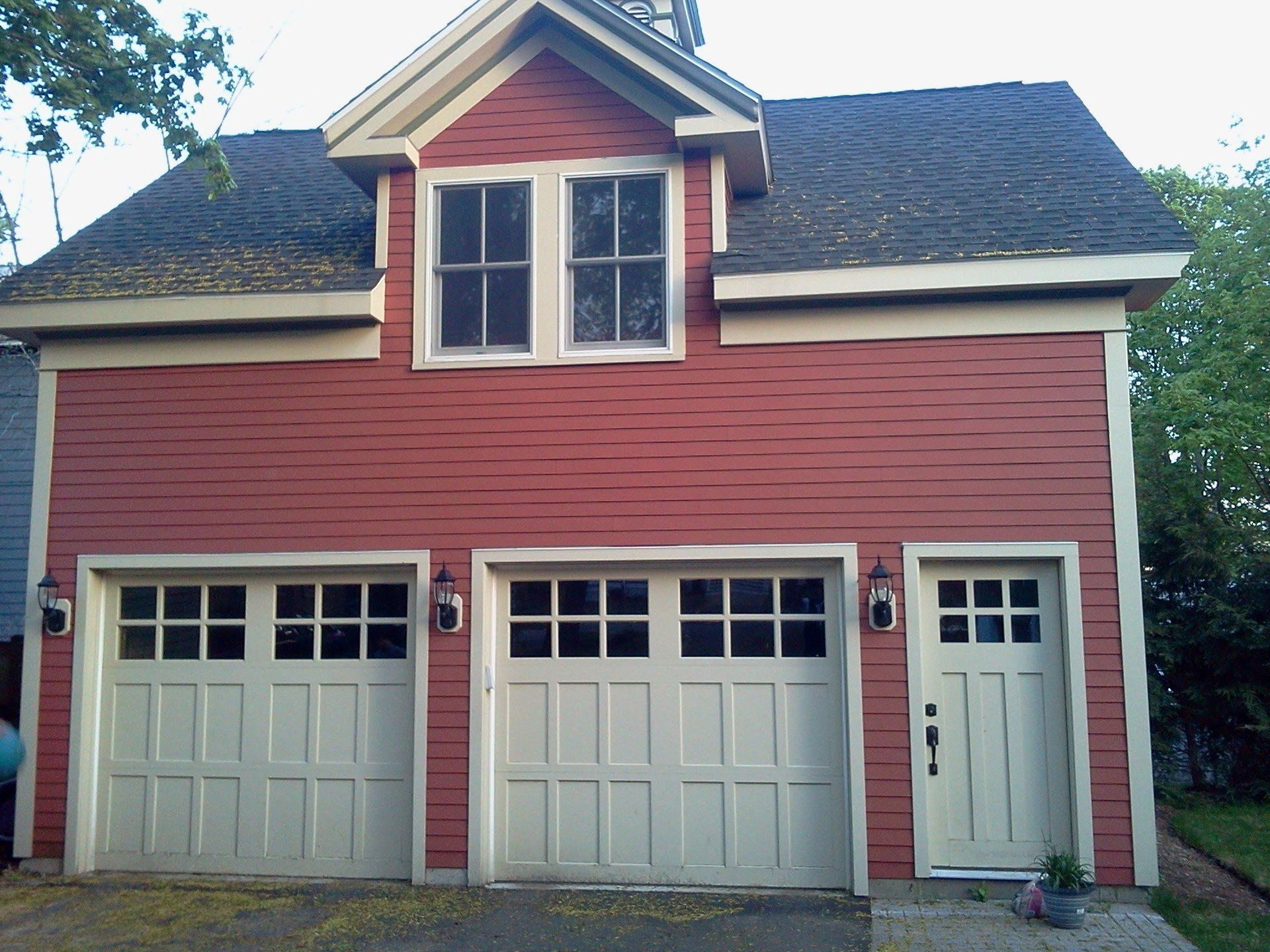 Red two-story house with three white garage doors and a small dormer window above.