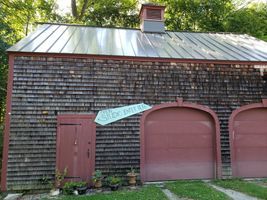 Old barn with weathered wood siding, metal roof, and two large pink garage doors under trees