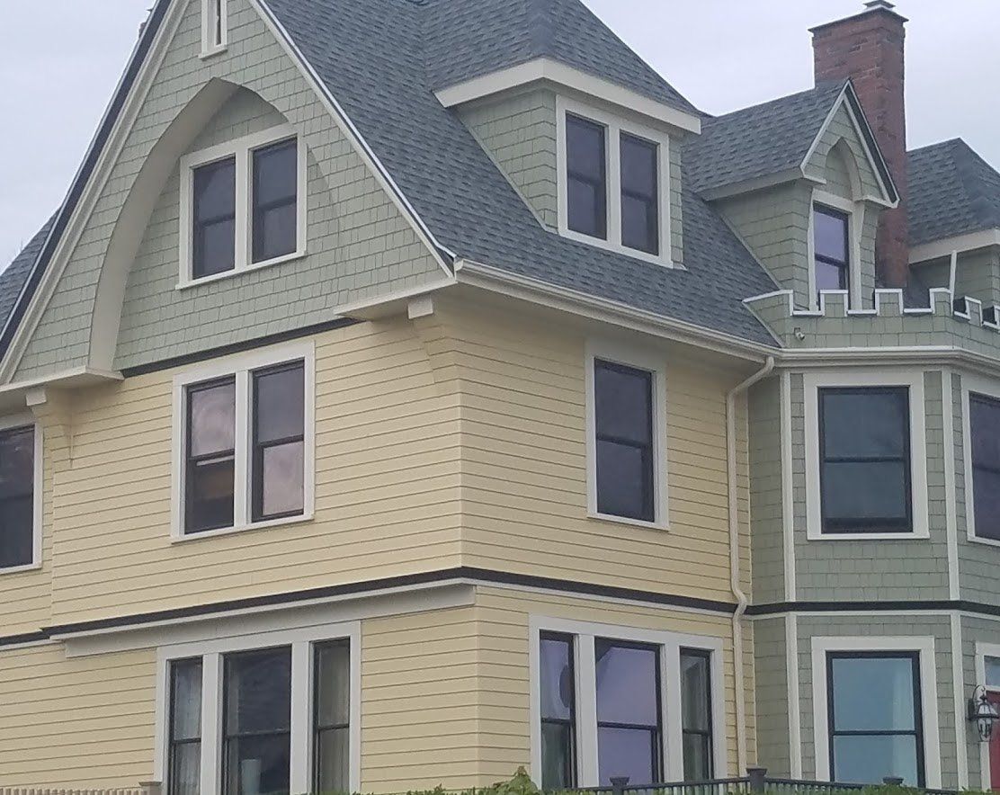 Victorian-style house with pale yellow siding, green trim, bay windows, and a steep gray roof