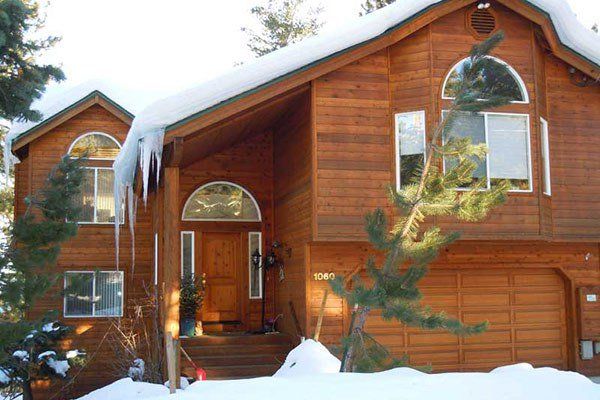 Two-story wood-paneled house with snow on the roof. Icicles hang from the eaves; a small evergreen tree is in front.Ice Dam | MasterCraft Roofing, Siding & Windows | Serving Eastern MA, NH & Selected Areas of VT
