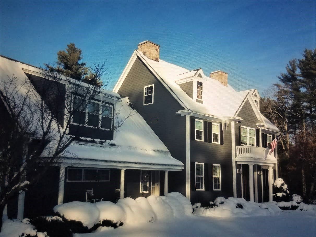 Snow-covered gray house with white trim under a clear blue winter sky