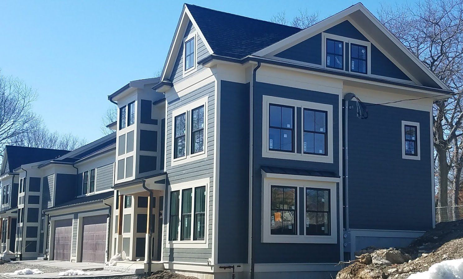 Modern two-story gray house with white trim and large windows in a snowy residential setting