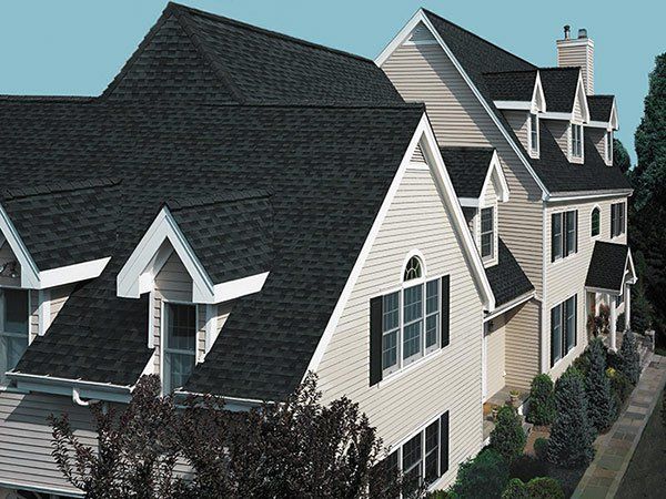 Dark shingled roof on a beige house with multiple dormers and black shutters. Roofing Repairs | MasterCraft Roofing, Siding & Windows | Serving Eastern MA, NH & Selected Areas of VT