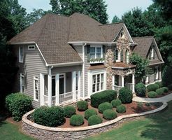 Suburban two-story beige house with brown roof, white trim, and neatly landscaped front yard.