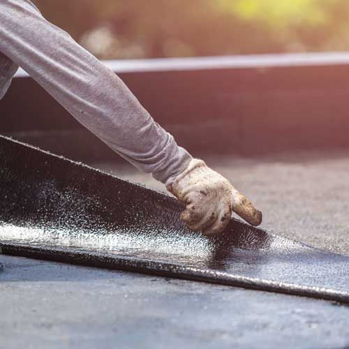 Person in work gloves installing roofing material. Roofing | MasterCraft Roofing, Siding & Windows | Serving Eastern MA, NH & Selected Areas of VT