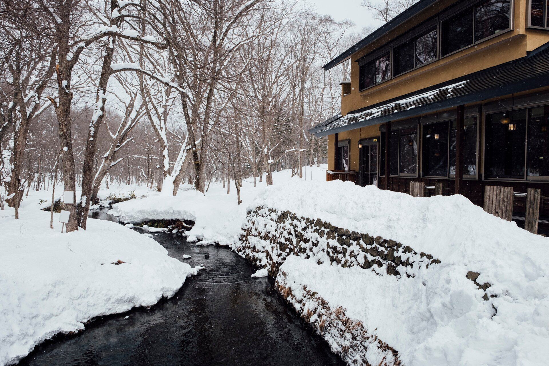 Snow-covered creek beside a wooden building in a winter forest