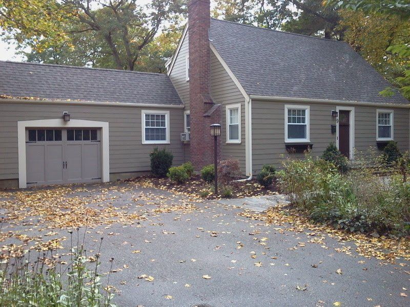 Tan house with a garage, dark roof, chimney, and driveway covered in fall leaves. Siding | MasterCraft Roofing, Siding & Windows | Serving Eastern MA, NH & Selected Areas of VT
