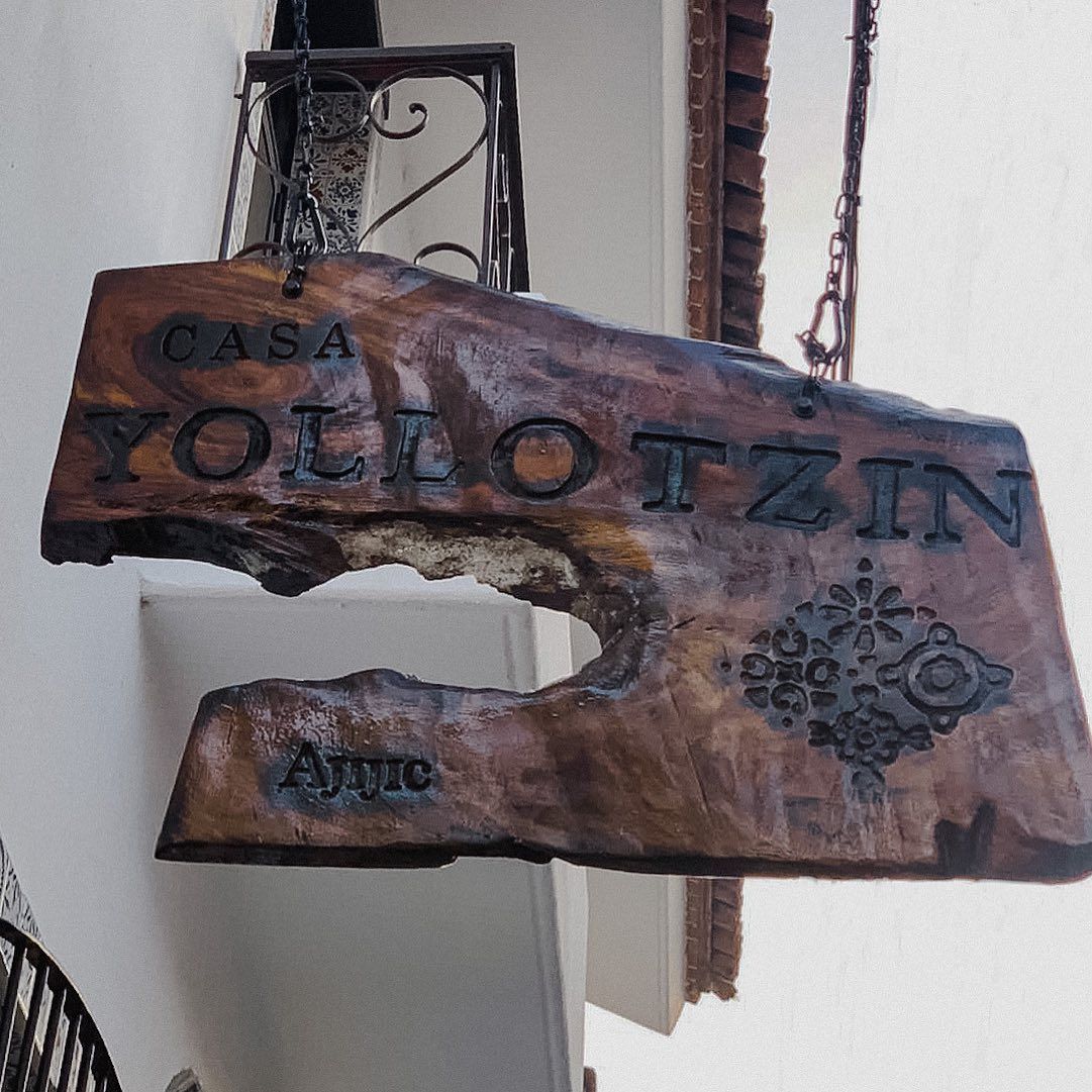 Un cartel de madera de Casa Yollotzin cuelga del costado de un edificio.