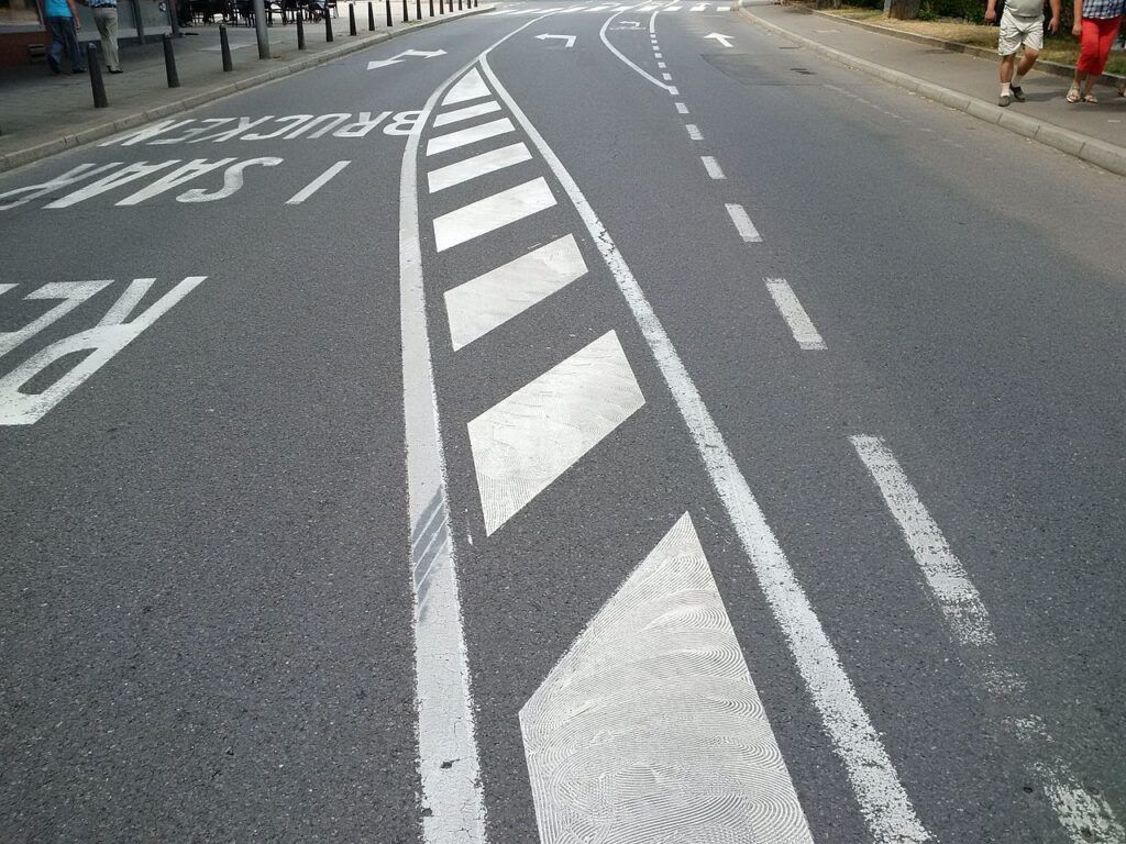 Roadway with painted white markings for lane separation and direction, including a chevron-patterned island.