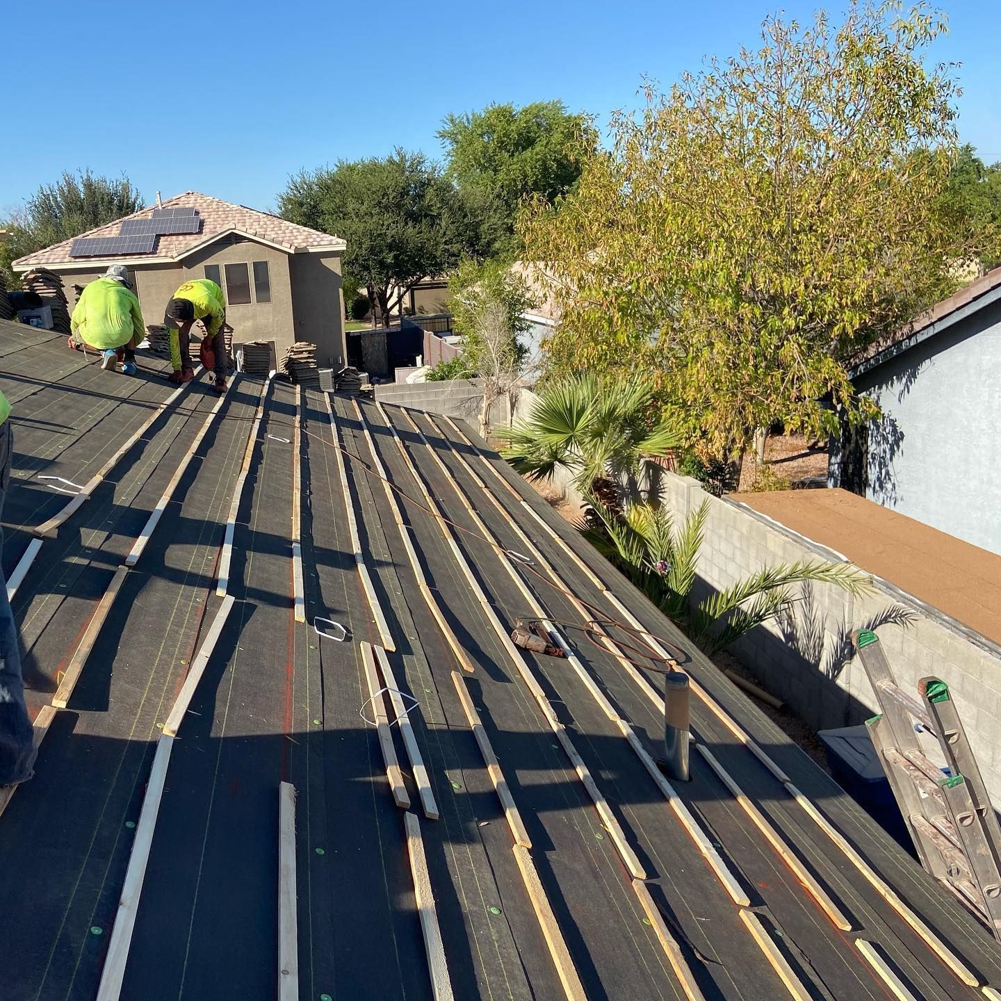 Construction workers replacing roof shingles on a house, sunny day.