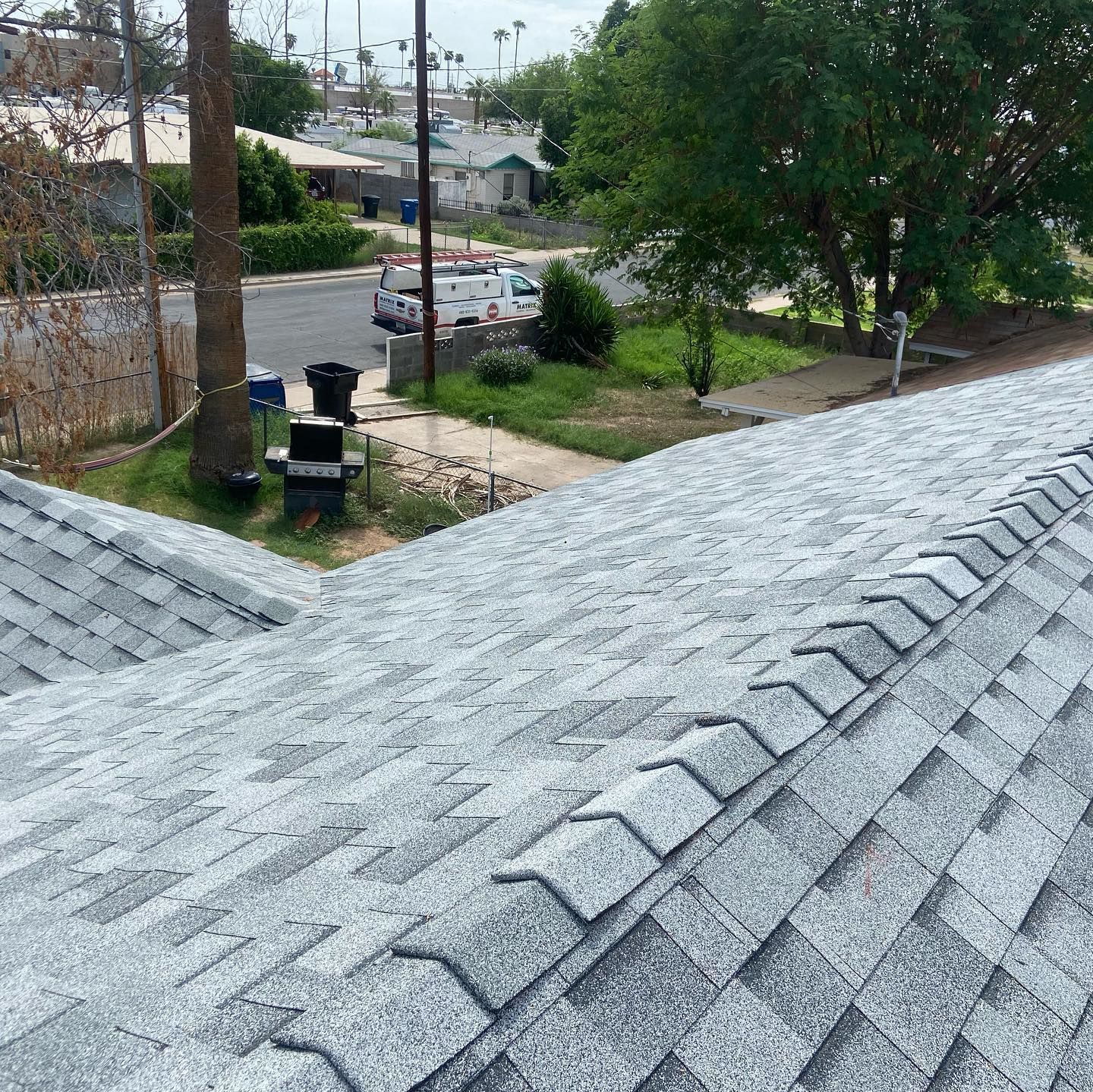 View of a grey shingled roof with a street and houses in the background.