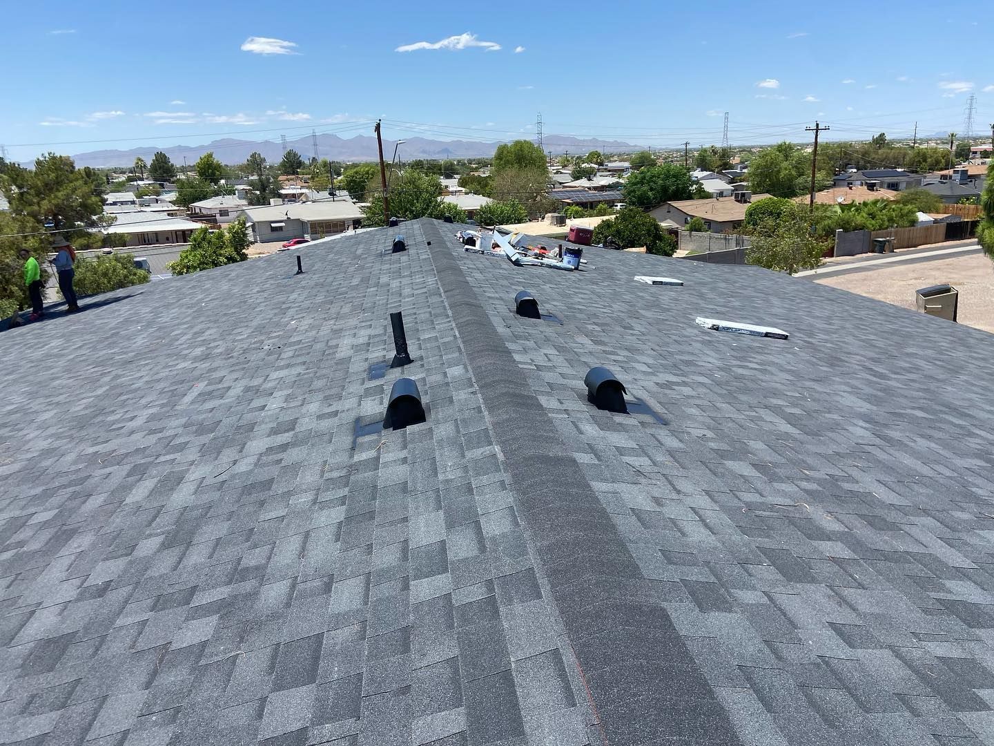 View of a newly shingled roof with several vents, in a suburban setting on a sunny day.