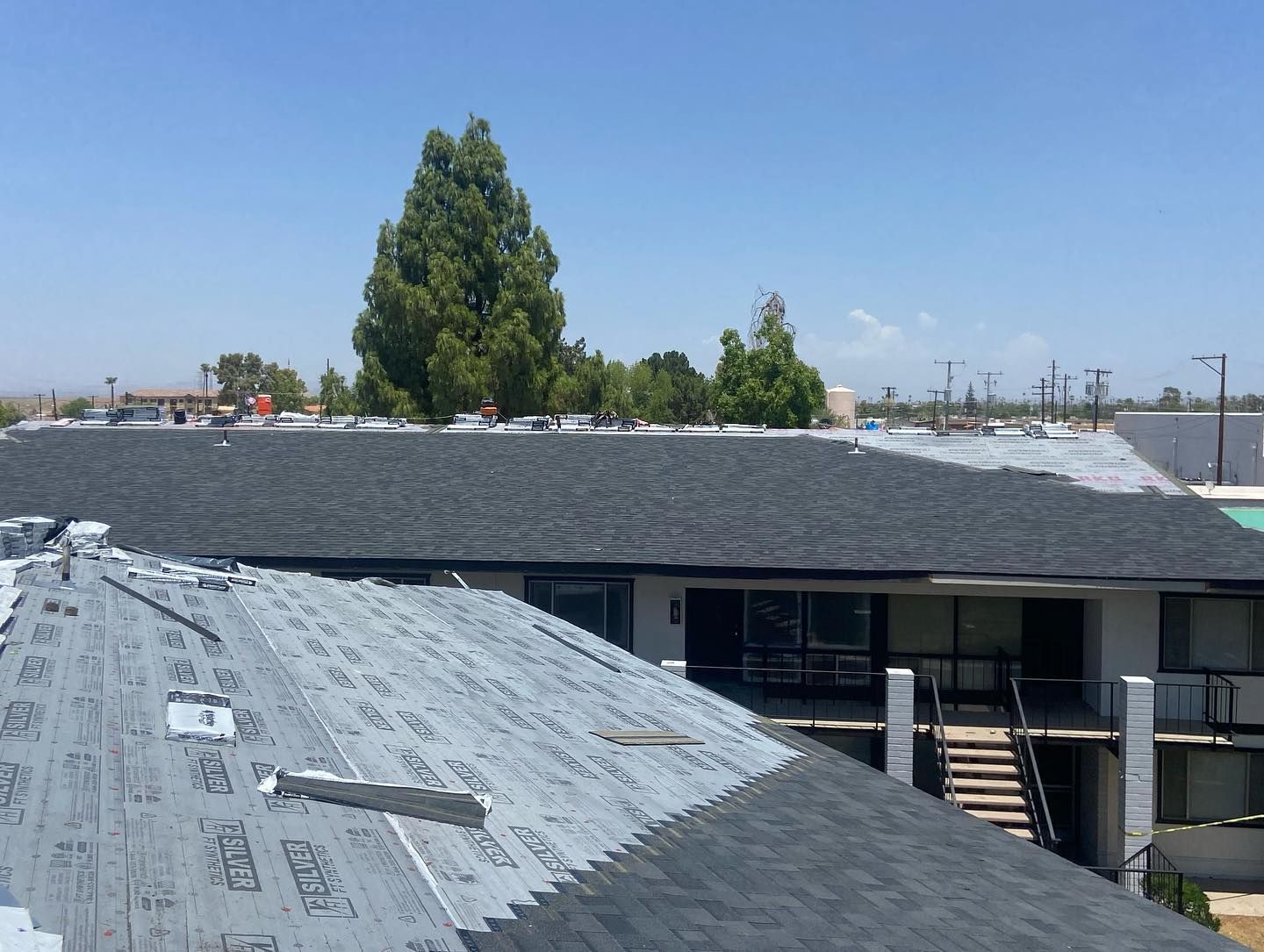 Roofing work in progress on a multi-story building, with new shingles being installed under a blue sky.