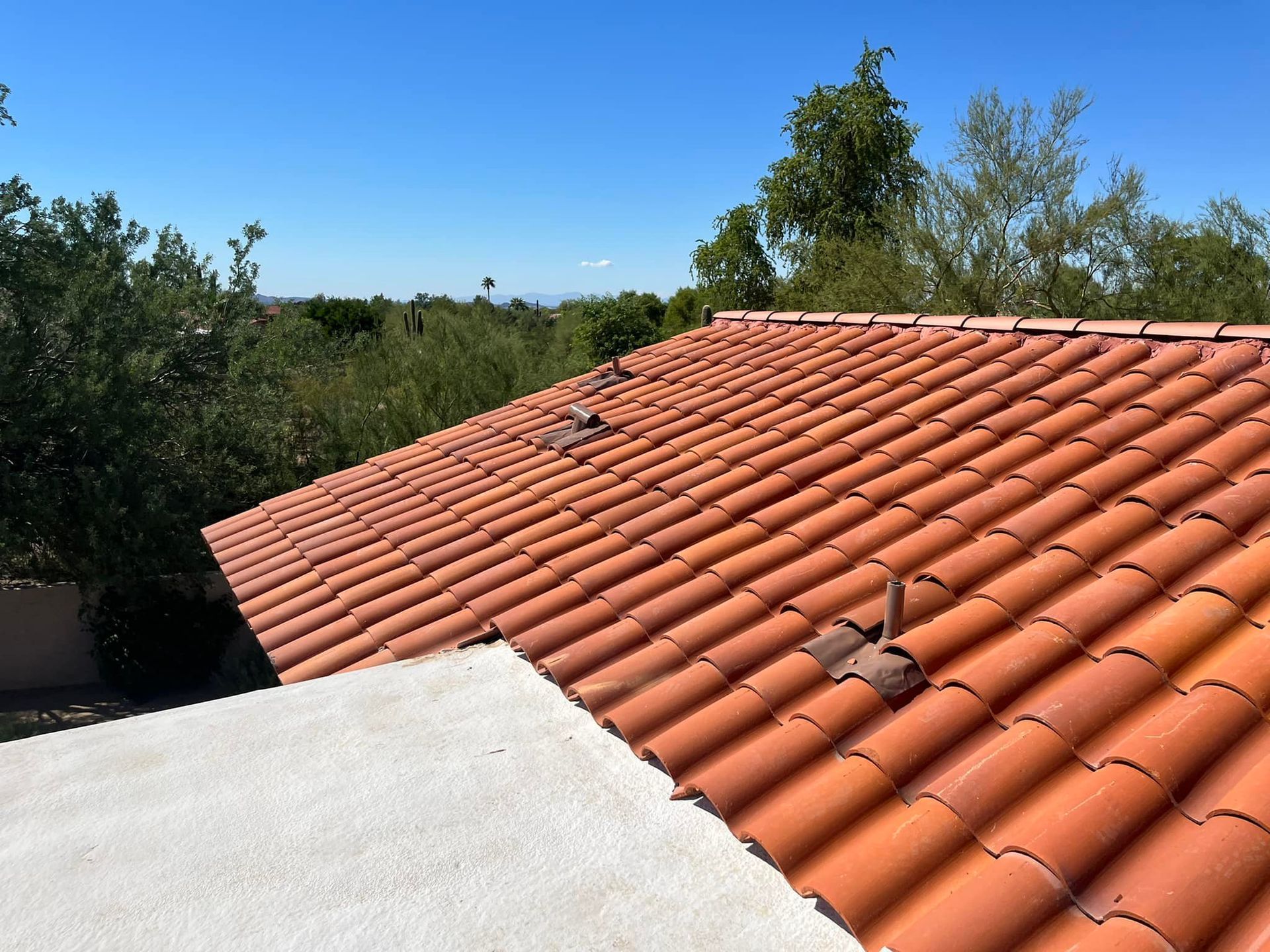 Red tile roof on a house, with a blue sky background and trees.