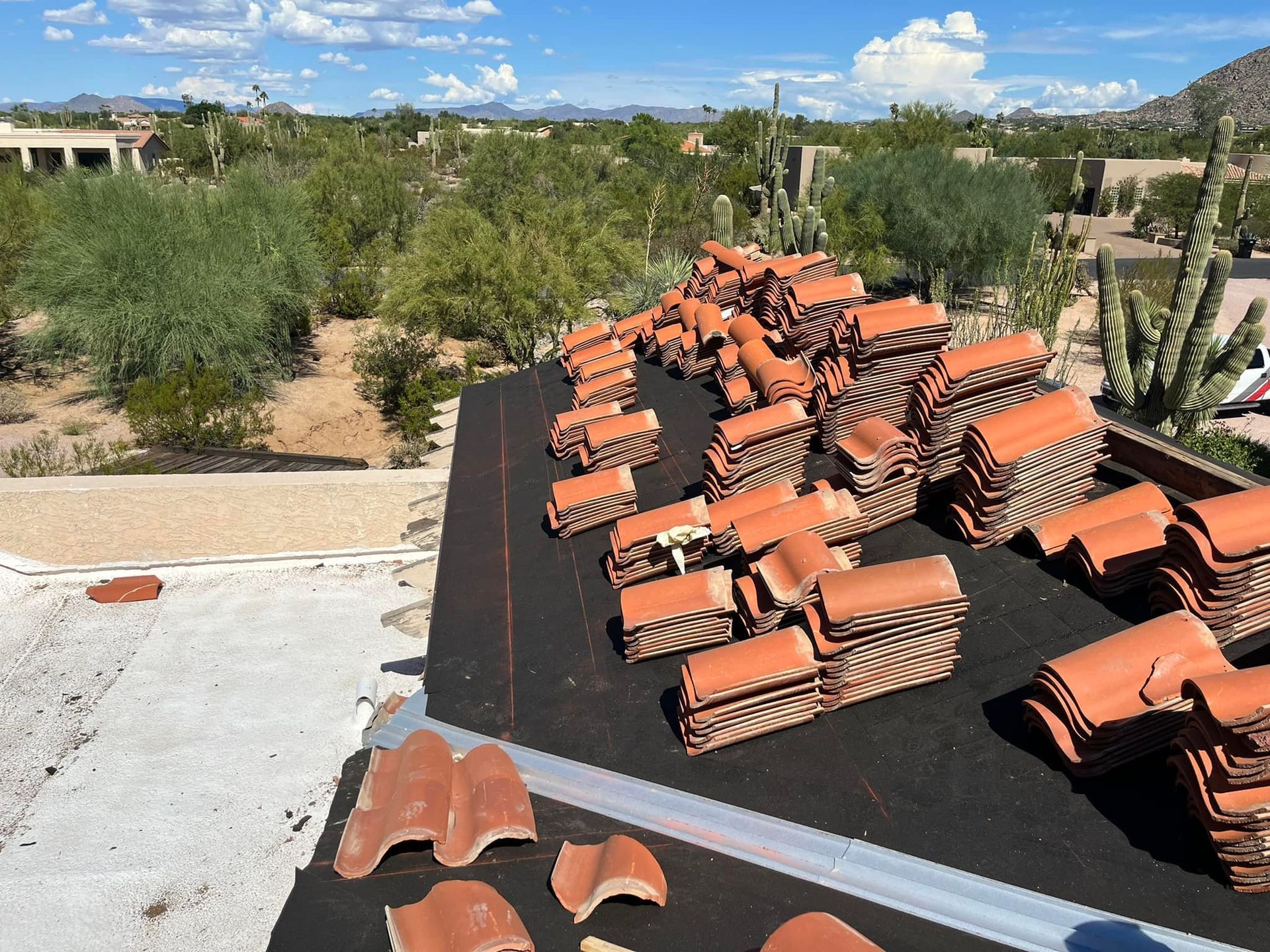 Stacks of red clay roof tiles on a flat roof with a scenic desert landscape in the background.