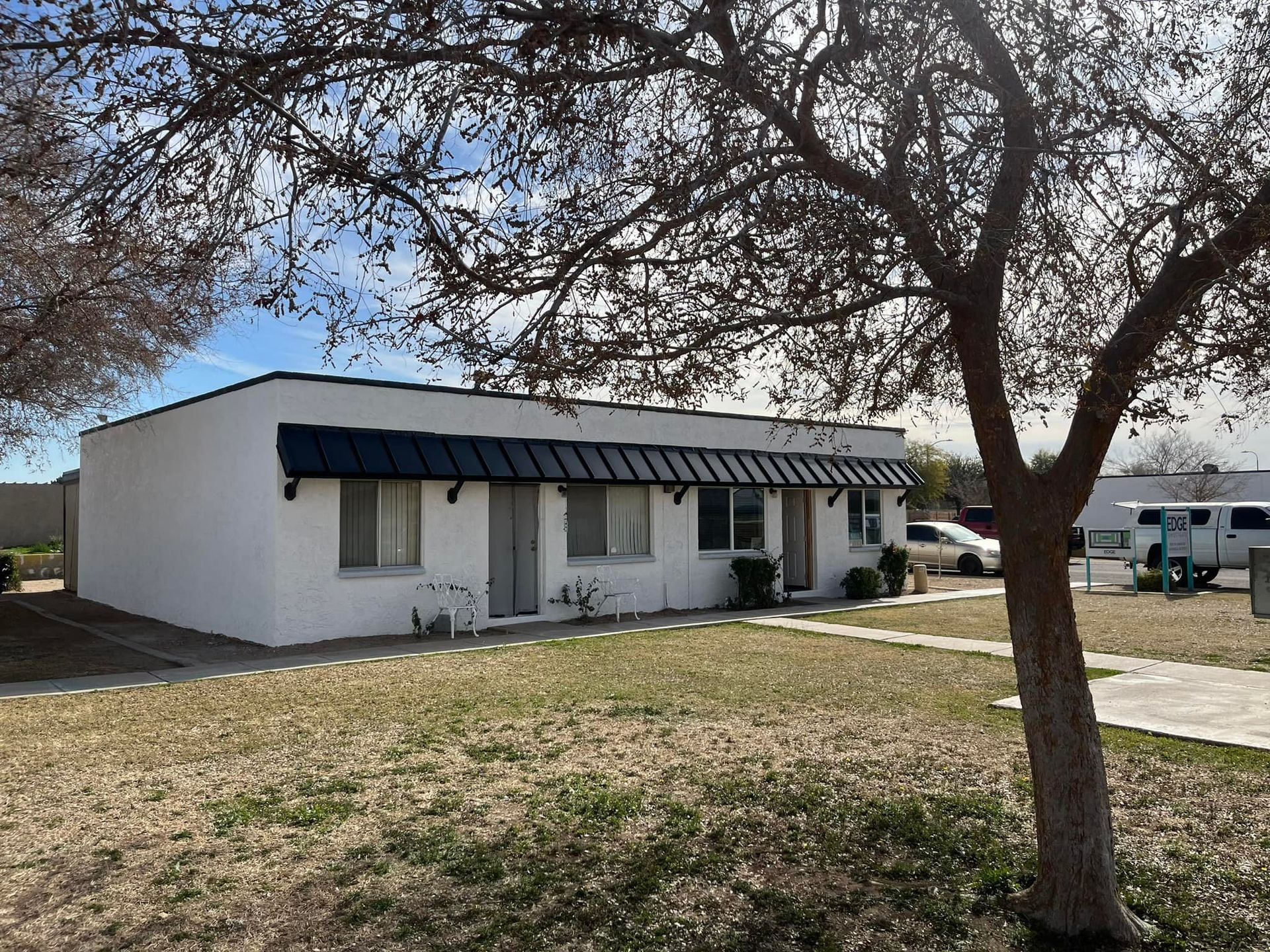 White stucco building with black awning and bare tree in front.
