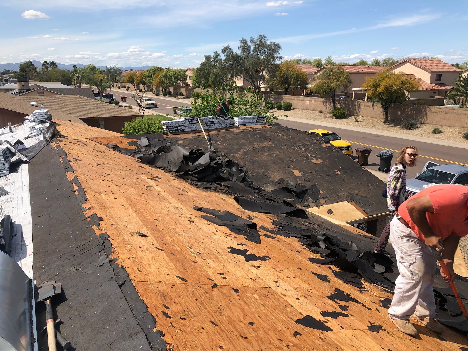 Workers remove old roofing material from a house in a residential area on a sunny day.