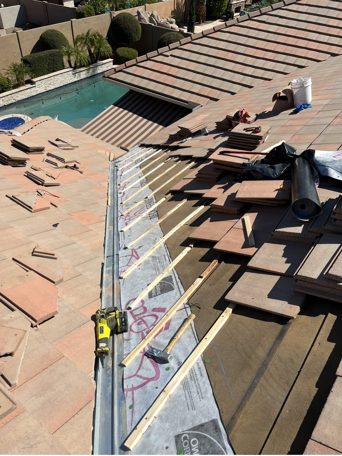Rooftop under construction with terracotta tiles. Saw, wood strips, and protective layer visible.