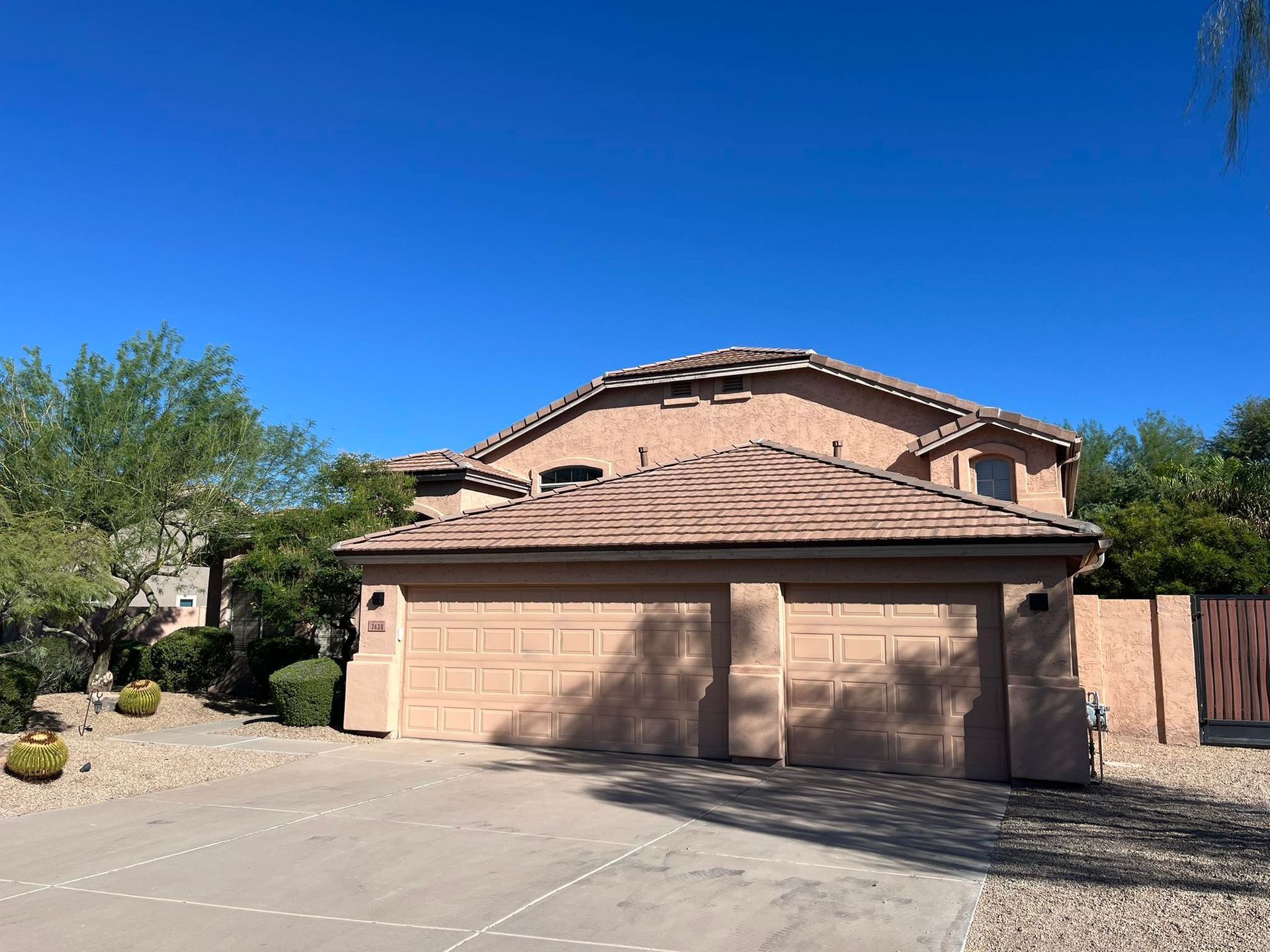 Two-story beige house with a three-car garage under a bright blue sky.
