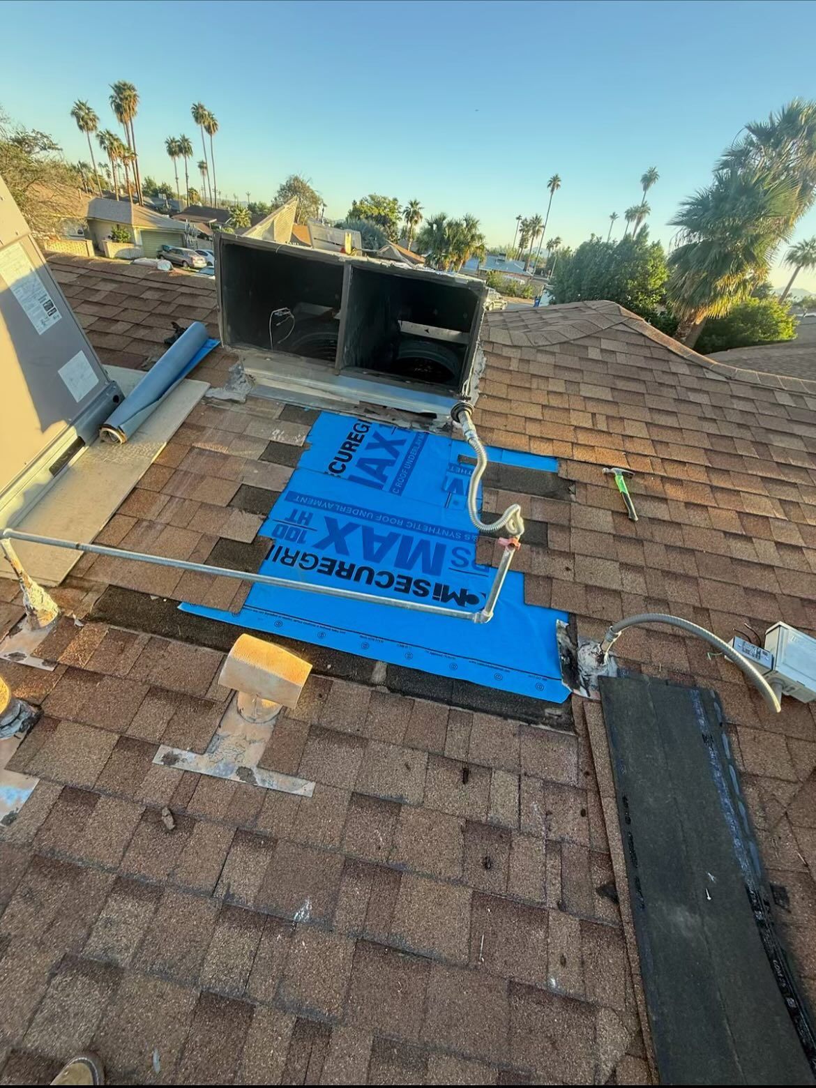 Rooftop with blue underlayment and vents, partially completed roof repair, with a sunny sky in the background.