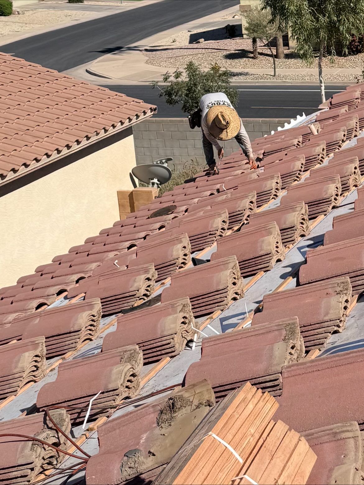 Roofer working on a terracotta tile roof, bundles of tiles at the bottom, beige house, street in background.