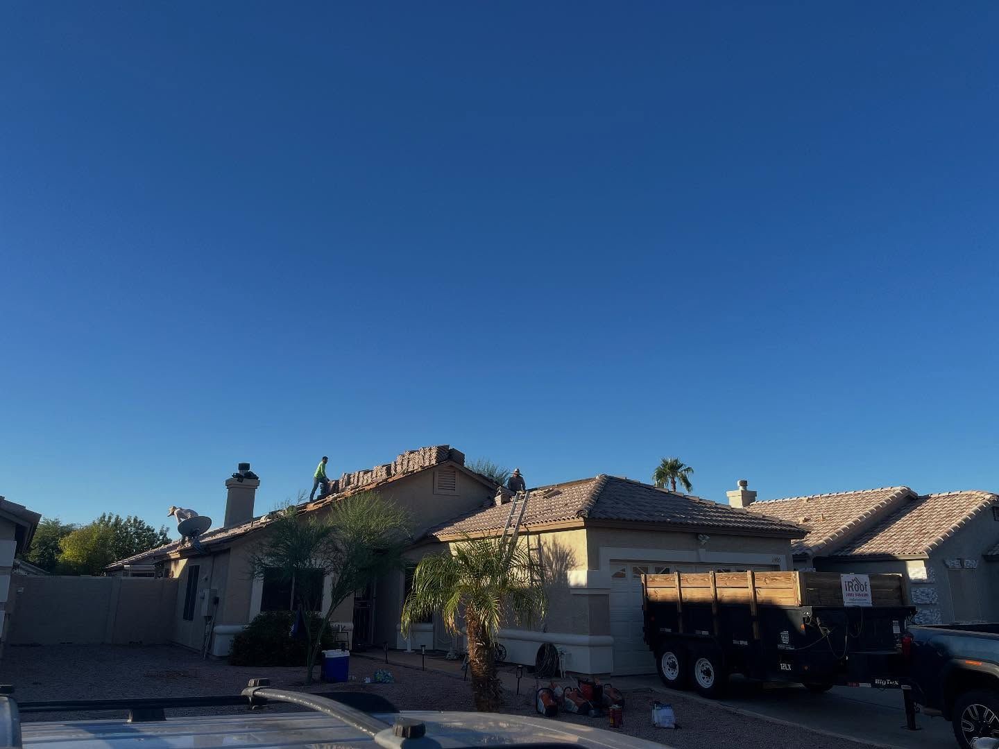 Workers on a roof with a trailer, house, palm tree, and a clear blue sky.