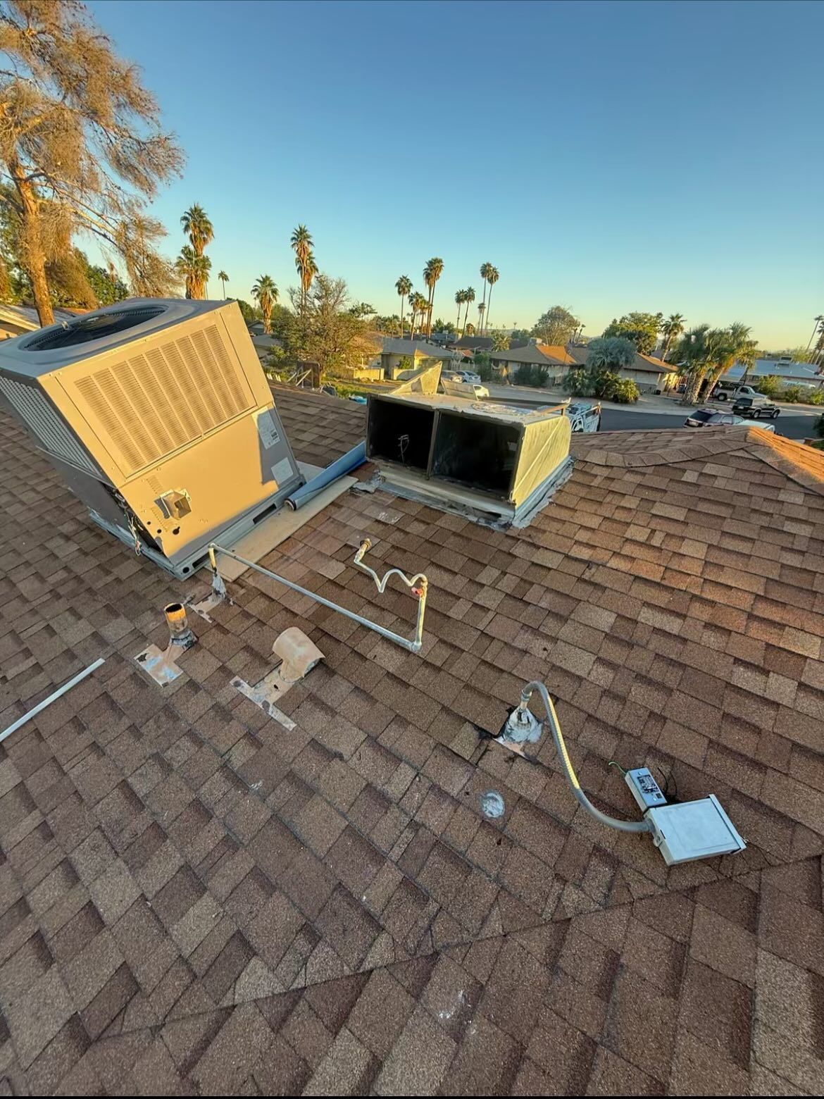 HVAC units on a rooftop with brown shingles and a clear blue sky in the background.