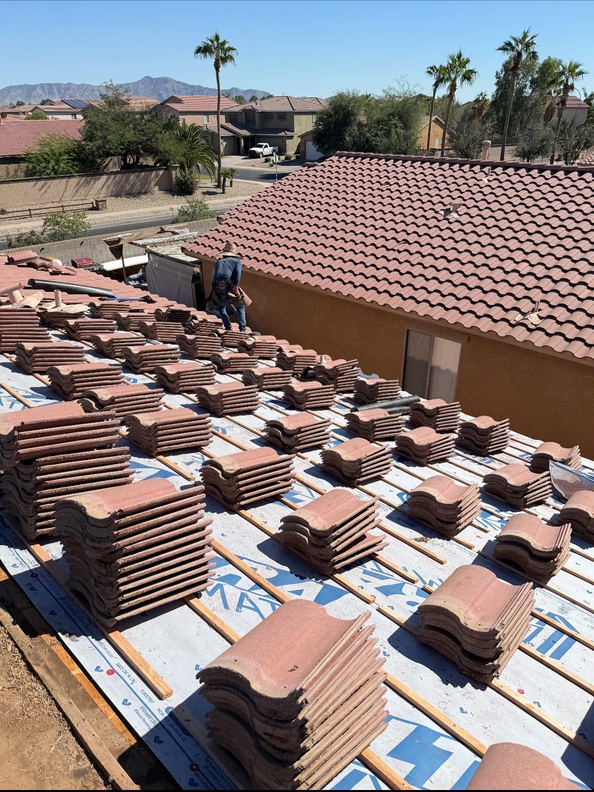 Roofer laying red roof tiles on a house. Tiles are stacked on roof. Bright sunny day.
