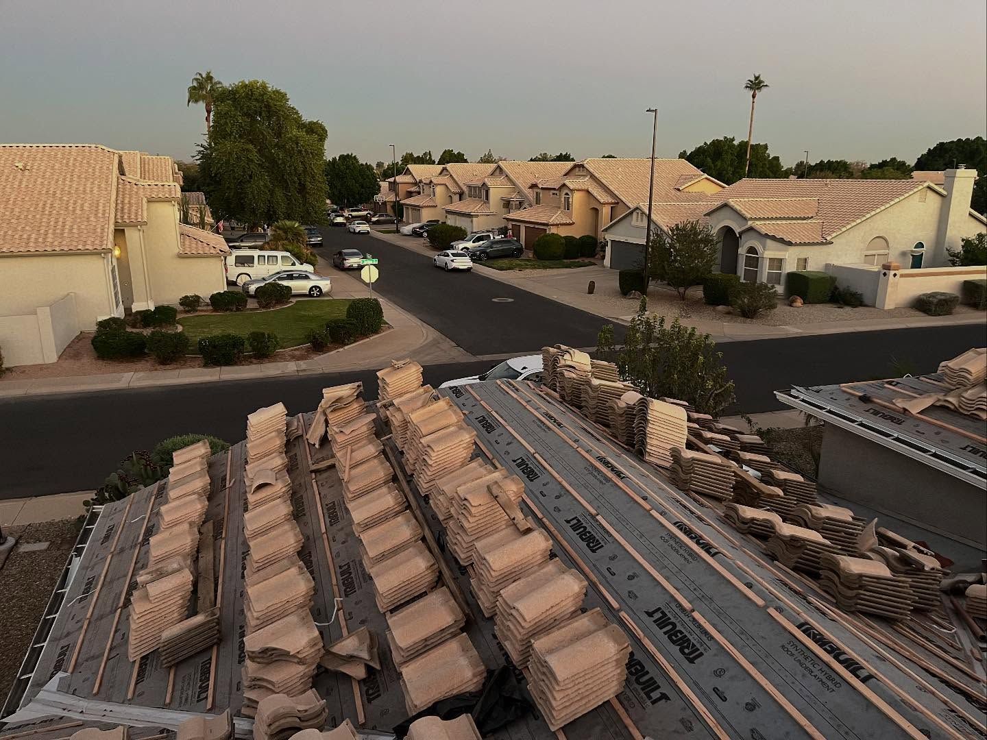 Rooftop construction with stacked tiles, overlooking a residential street with houses and vehicles.