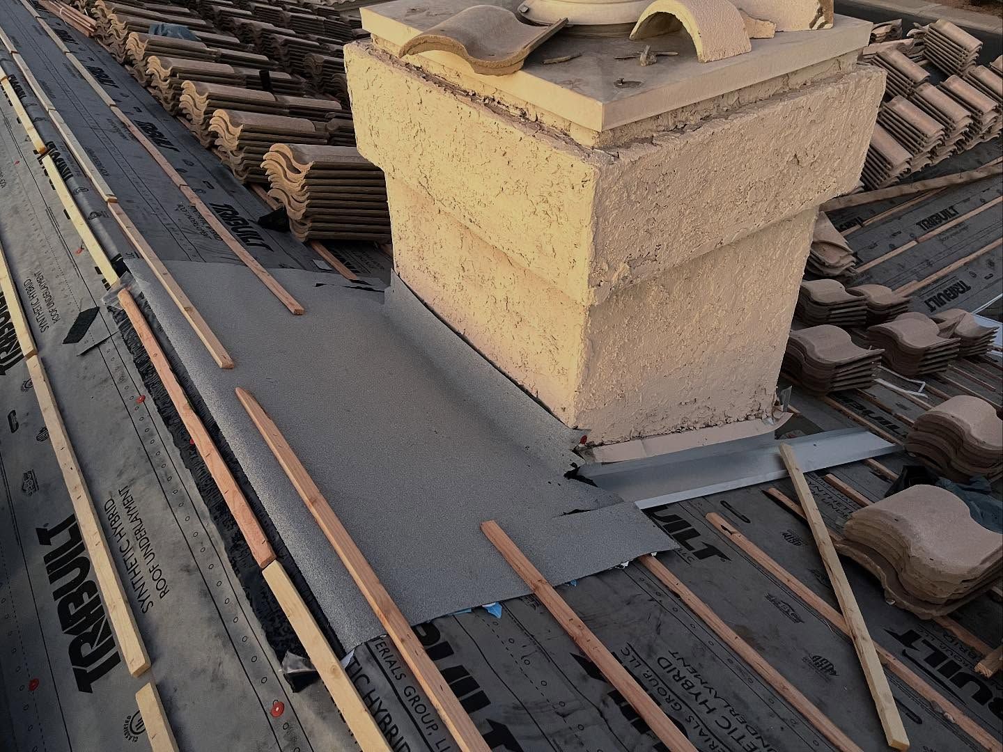Roof under construction with chimney, tiles, and wooden supports.