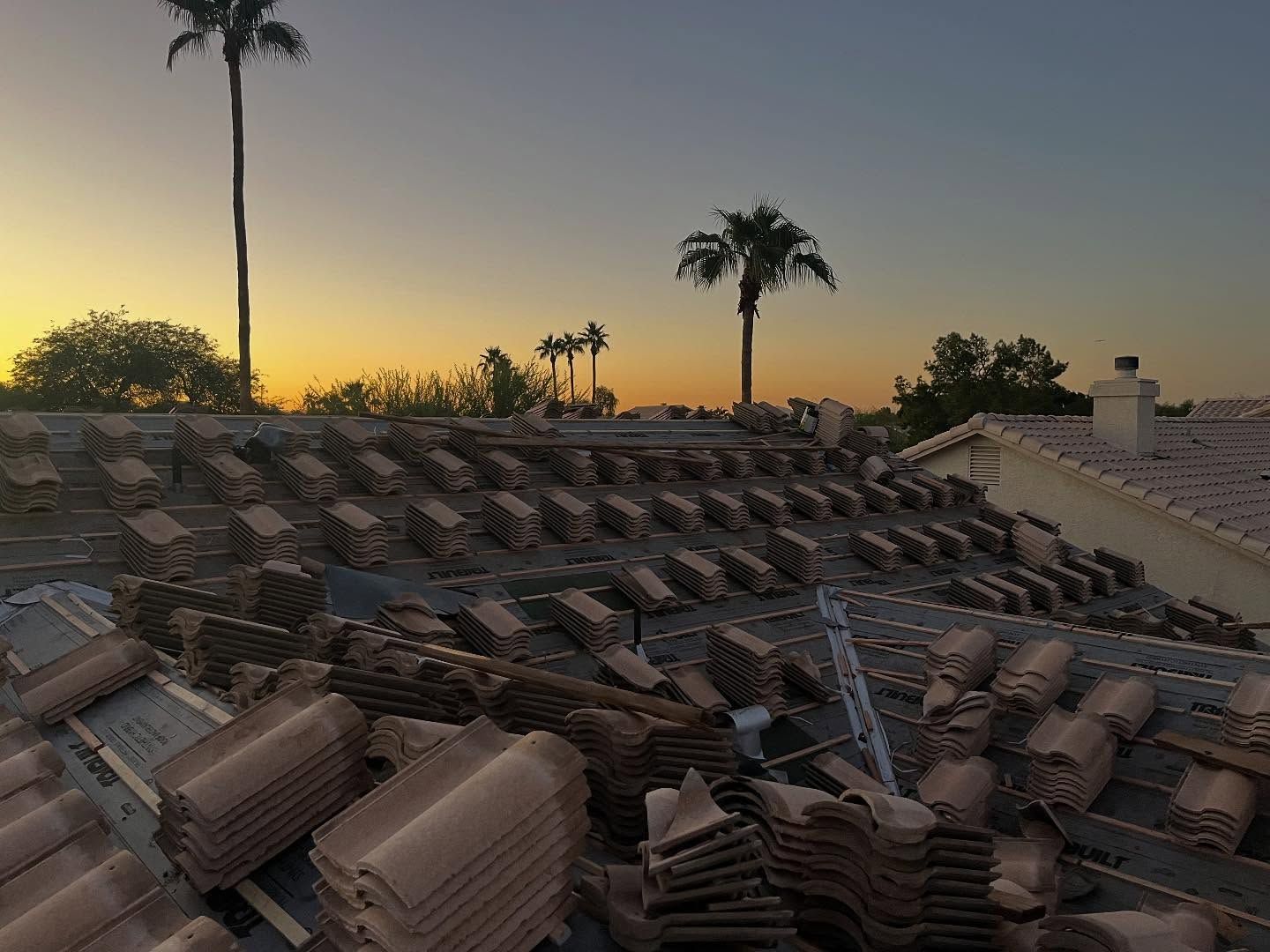 Roof with stacked clay tiles, sunset in background, palm trees visible.