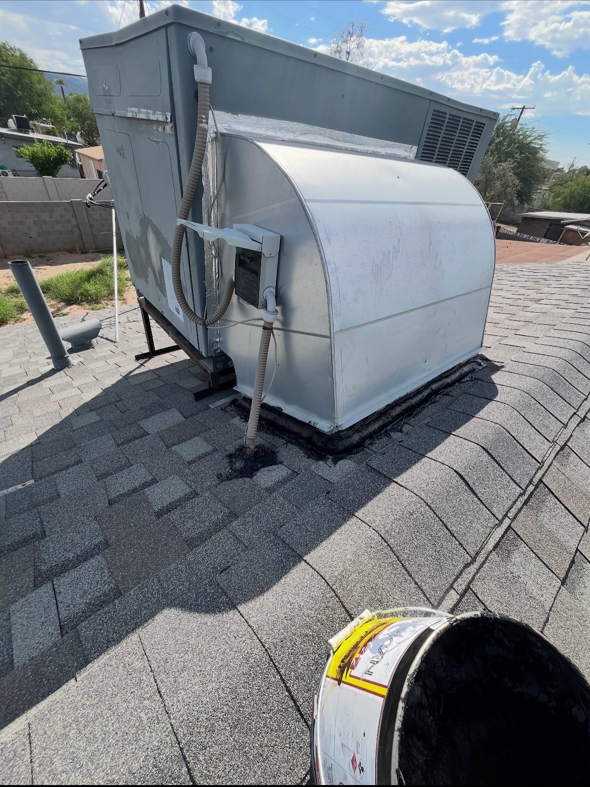 A large, metal HVAC unit on a gray shingle roof under a bright sky.