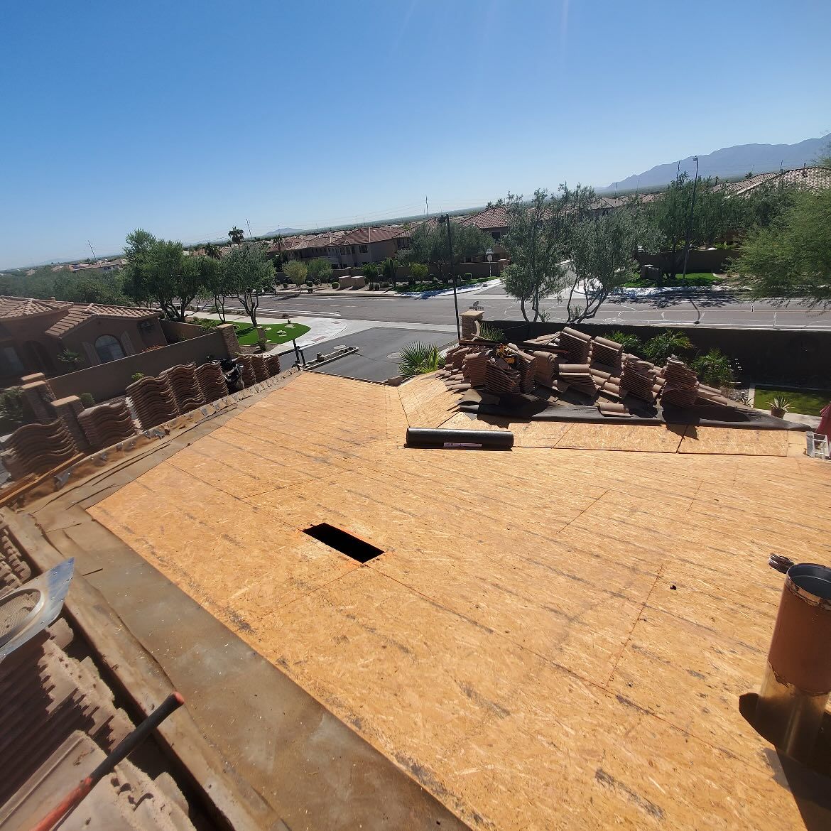 Roof with exposed plywood, overlooking a street and buildings on a sunny day.