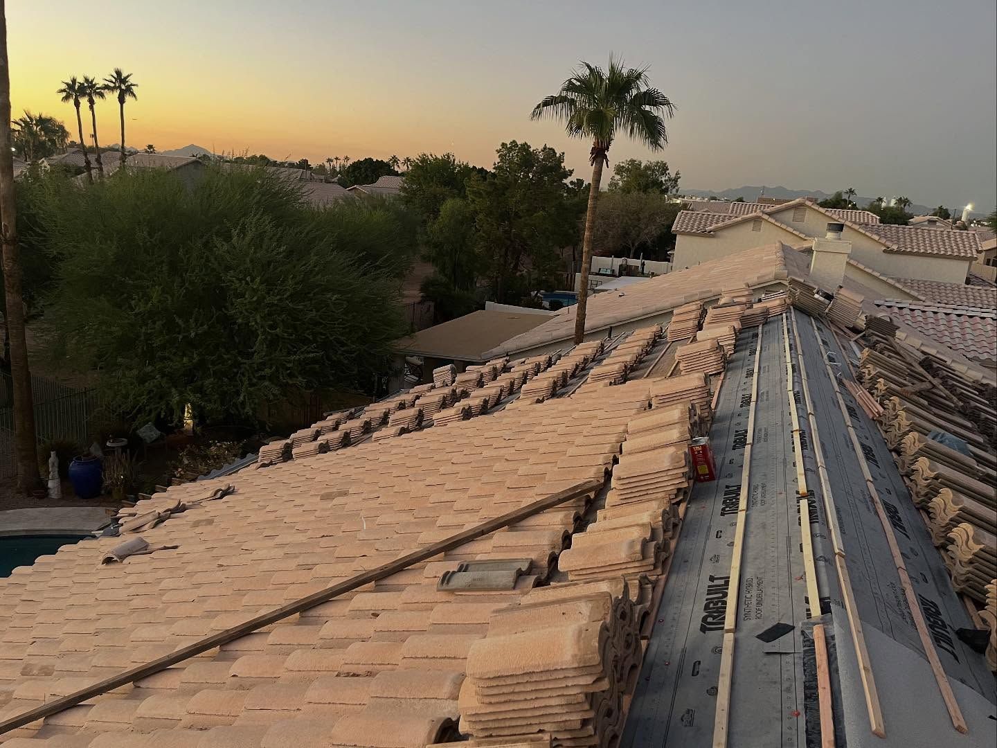 Roof of a building partially covered with new tiles during sunset. Palm trees and other homes visible.