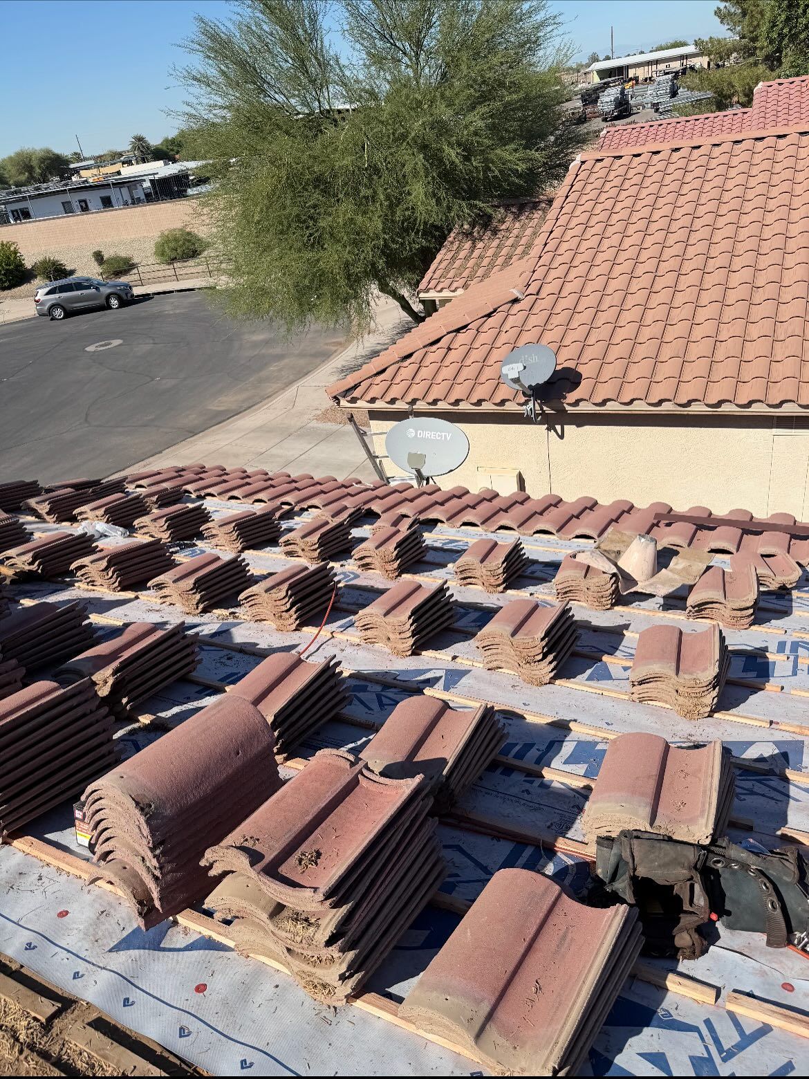 Roof with stacked terracotta tiles, wood frame, and building in the background. Sunny day.