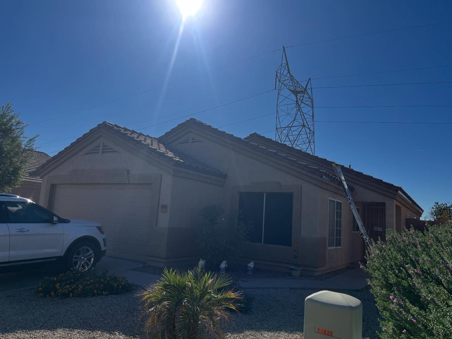 Tan house under a bright sun, with power lines visible behind. A white car is parked in front.