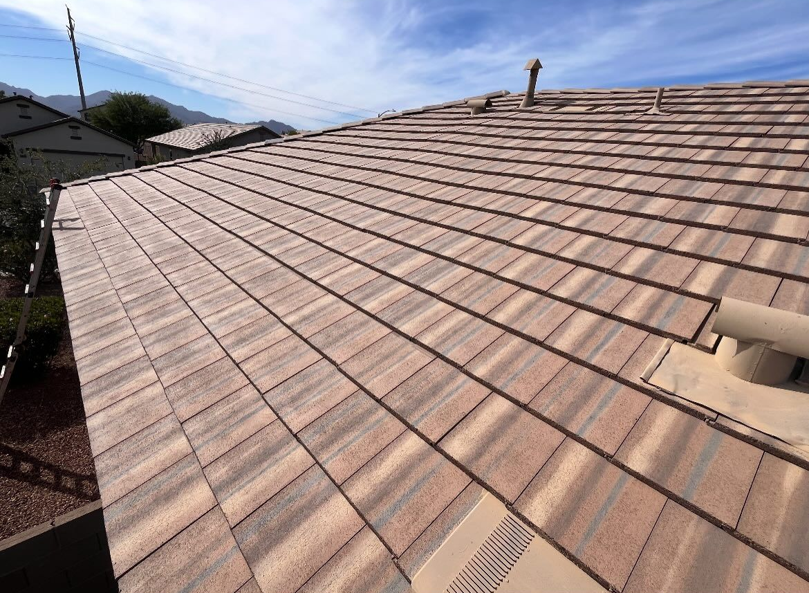 Brown and tan roof tiles on a house under a partly cloudy blue sky.