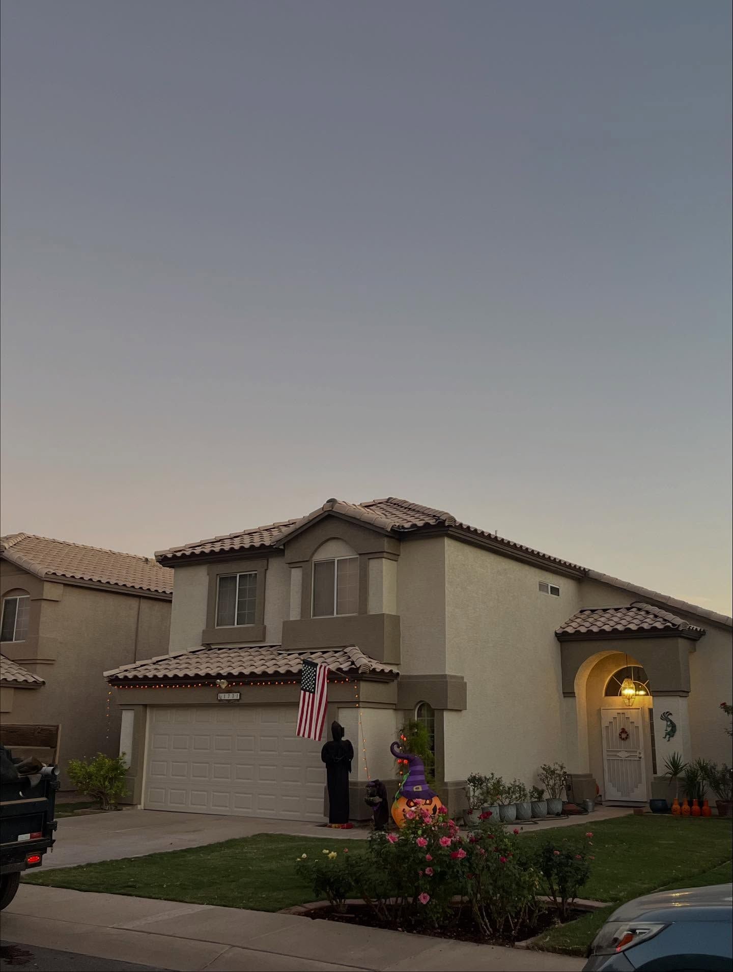 Two-story beige house with garage, American flag, and Halloween decorations on lawn at dusk.