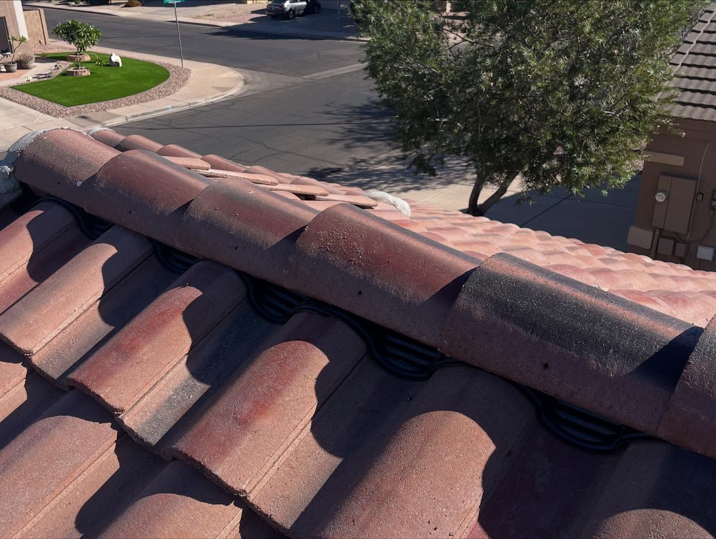 Red clay roof tiles with visible black underlayment, viewed from an upward angle on a sunny day.