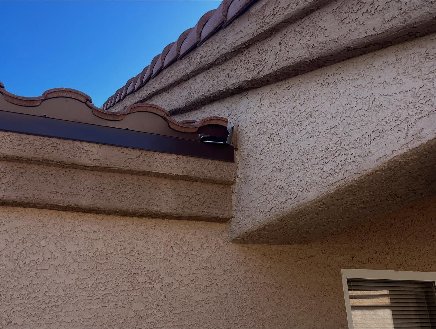Brown roof tiles and trim on a stucco building against a blue sky.